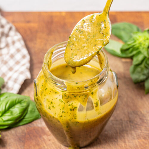 Spoon with basil honey mustard dressing dripping over a jar.