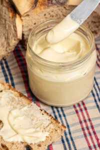 Homemade mayonnaise in a jar with a knife over it and a slice of bread with mayo on top.