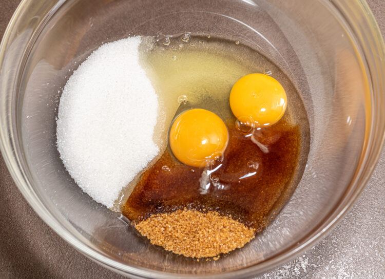 Glass bowl with two eggs, white and brown sugar.