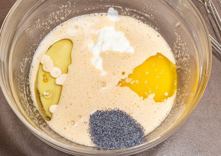 Bowl with foamy mixture, yogurt, oil, and poppy seeds.