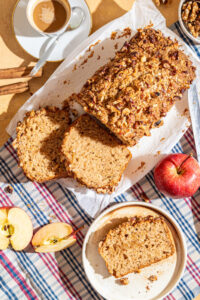 Sliced apple walnut loaf cake with one slice on a plate and apples on the side.