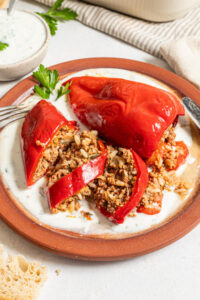 Sliced beef and rice stuffed pepper on a plate with yogurt sauce.