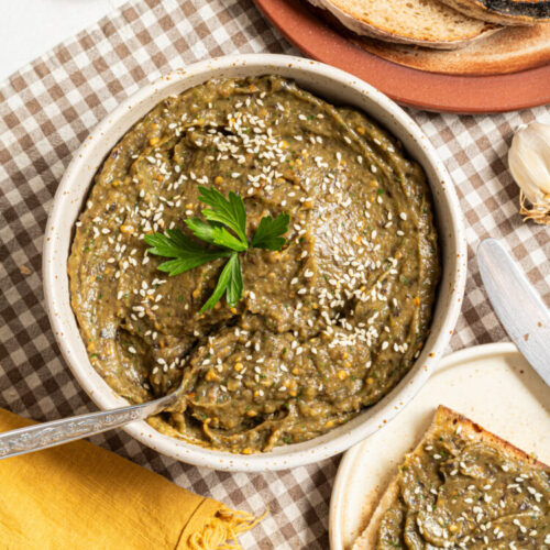 Roasted veggie spread in a bowl with a side of bread.