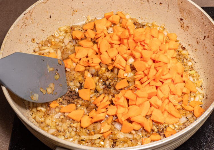 Chopped carrots added to a skillet with cooked onion.