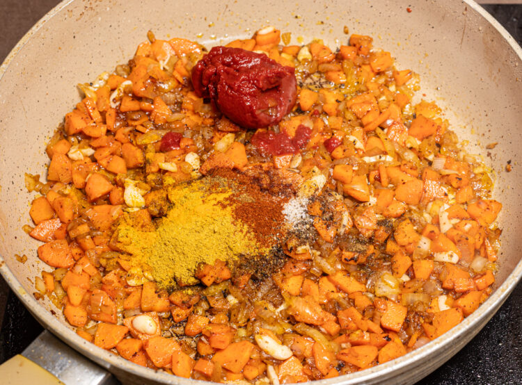 Spices and tomato paste added to a skillet with cooked onion and carrots.
