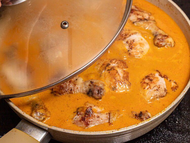 Covering a skillet with chicken curry with a lid.