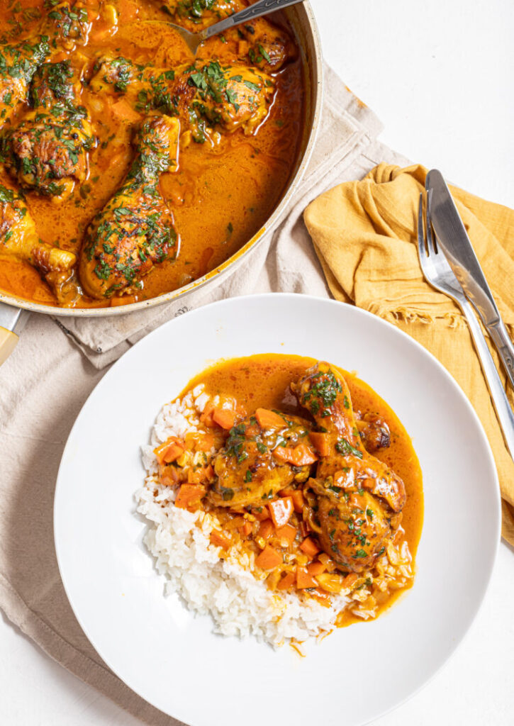 Chicken coconut curry on a plate with rice with a skillet on the side.