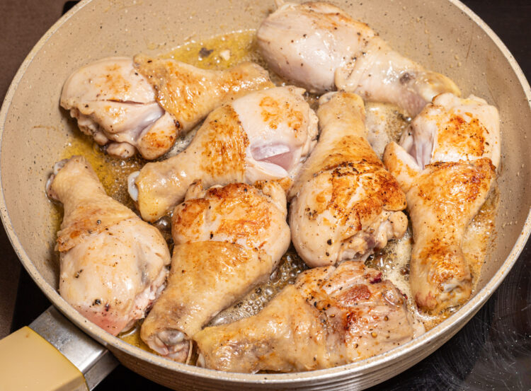 Browned chicken drumsticks in a skillet.