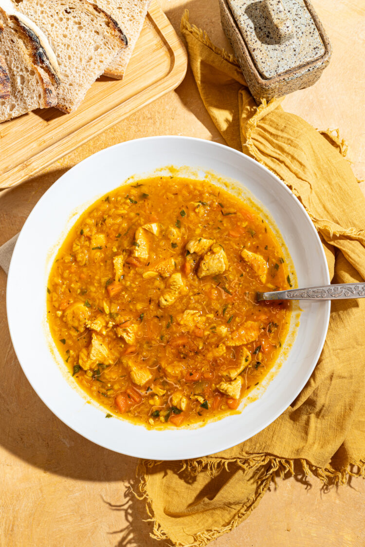 Red lentil soup with chicken in a bowl with a side of bread.