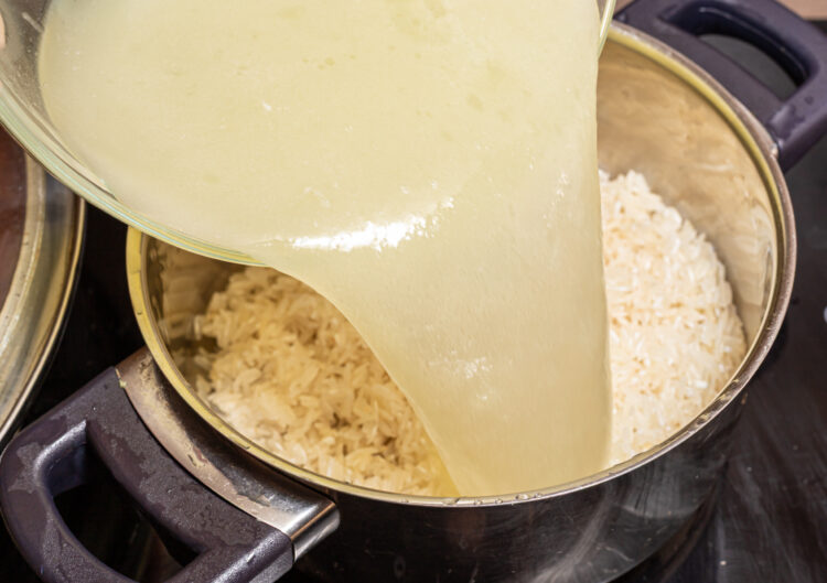 Adding chicken stock to a pot with rice.