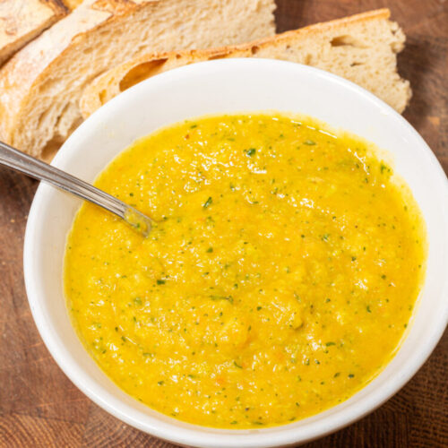 Root vegetable soup with broccoli and pear in a bowl with a spoon and bread on the side.